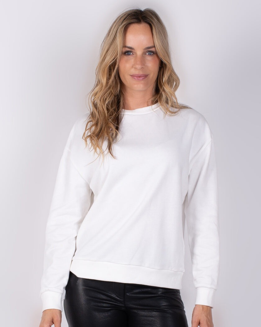 Vrouw poseert in witte sweater en zwarte leren broek uit Studio AW25-26 collectie.