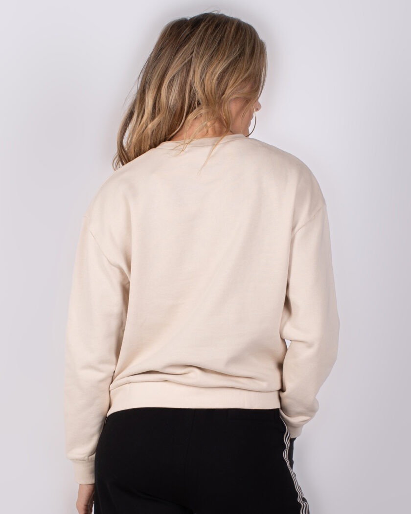 Achteraanzicht van een vrouw die een beige sweater en zwarte broek met witte strepen draagt.
