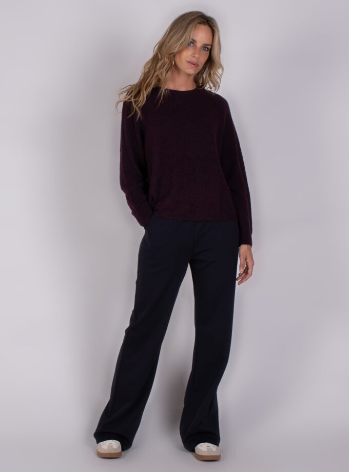 Vrouw draagt een donkerpaarse trui en donkere wijde broek uit de Studio AW25-26 collectie.