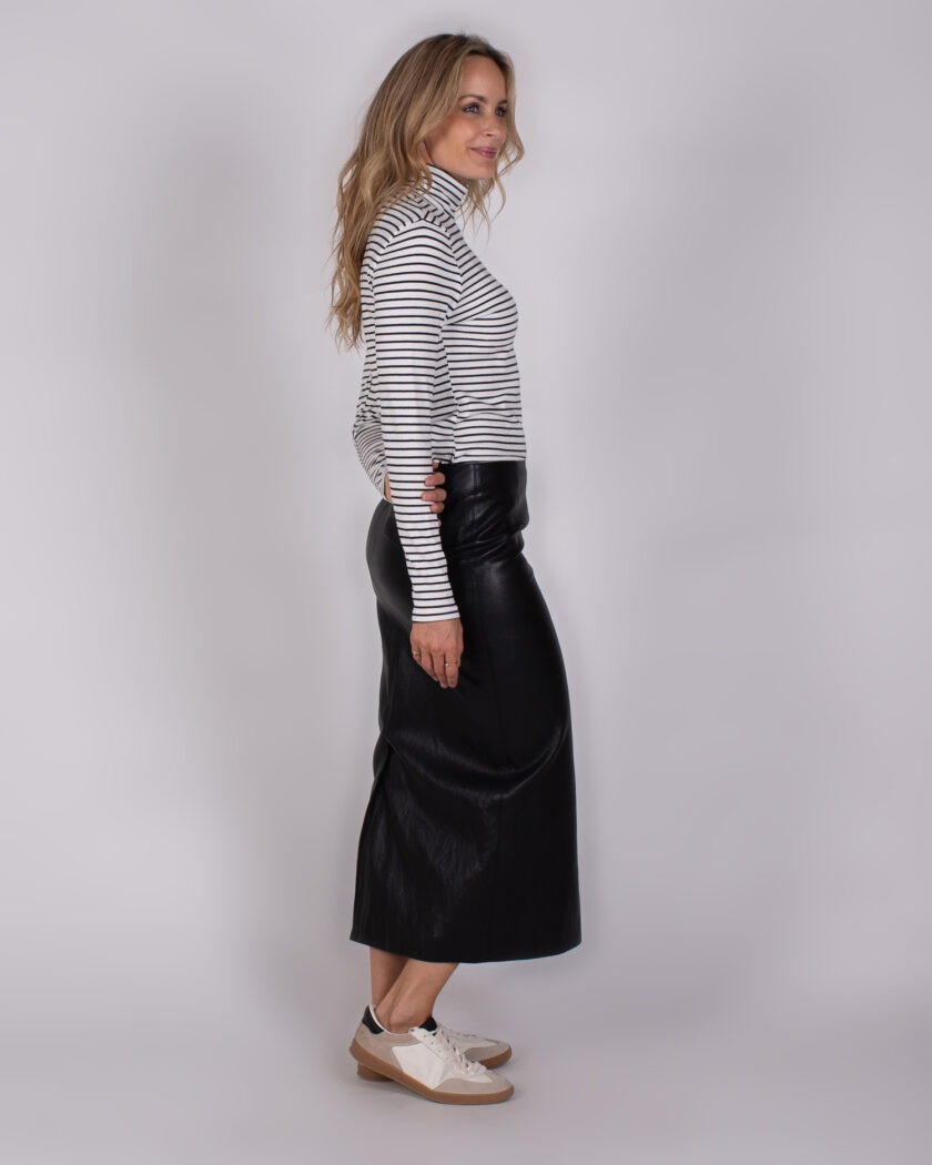 Vrouw in zijaanzicht draagt een gestreepte coltrui, zwarte leren rok en witte sneakers.
