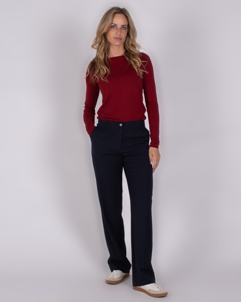 Vrouw draagt een bordeauxrode lange mouwtop en donkerblauwe pantalon uit de Studio AW25-26 collectie.