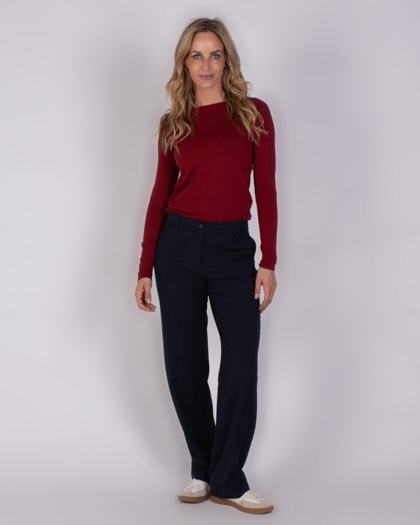 Vrouw in een rode lange mouwtop en donkerblauwe broek uit de Studio AW25-26 collectie.