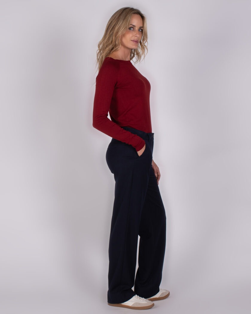 Vrouw in studio poseert in een bordeauxrode top en donkerblauwe wijde broek met witte sneakers.
