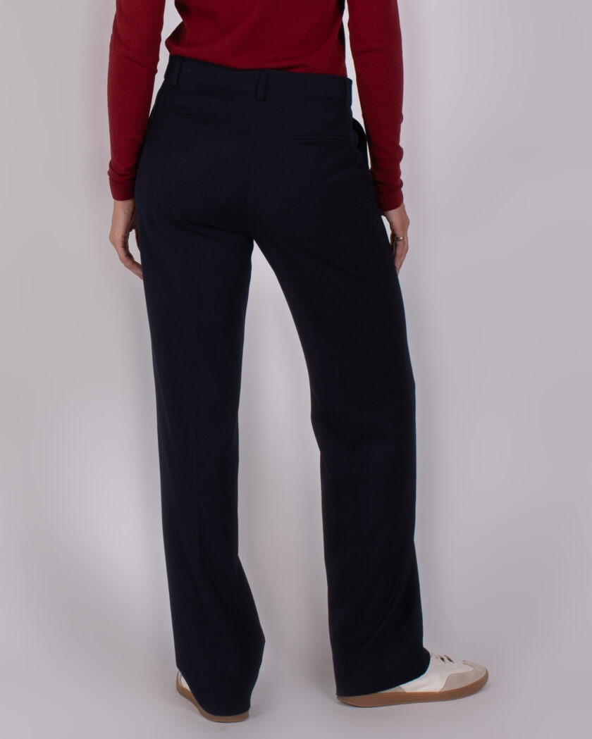 Achteraanzicht van een persoon in een rode top en donkerblauwe pantalon uit de Studio AW25-26 collectie.