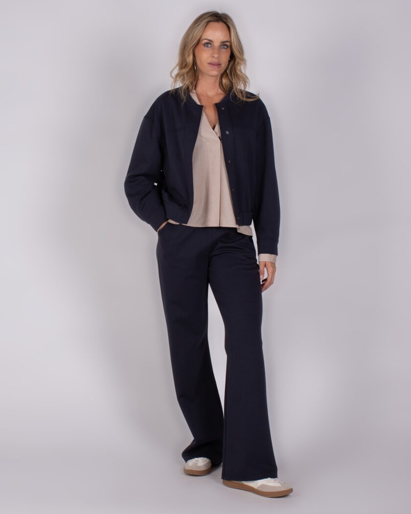 Vrouw draagt een donkerblauw Studio AW25-26-103 broekpak met beige top en casual schoenen.