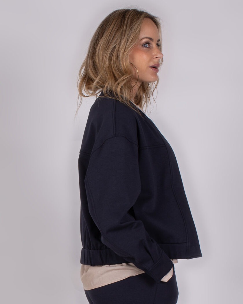 Vrouw in profiel draagt een donkerblauw jasje uit de Studio AW25-26 collectie.
