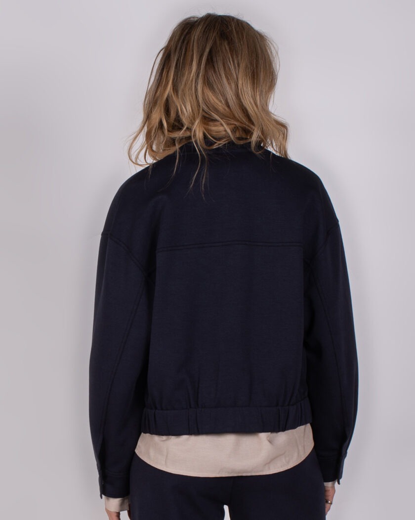 Achteraanzicht van een model dat een donkerblauw jack uit de Studio AW25-26 collectie draagt.