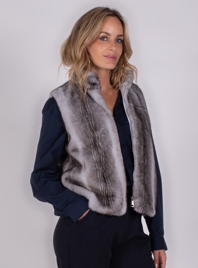 Vrouw draagt een chique grijze bont-look bodywarmer uit de Studio AW25-26 collectie over een donkerblauwe blouse.