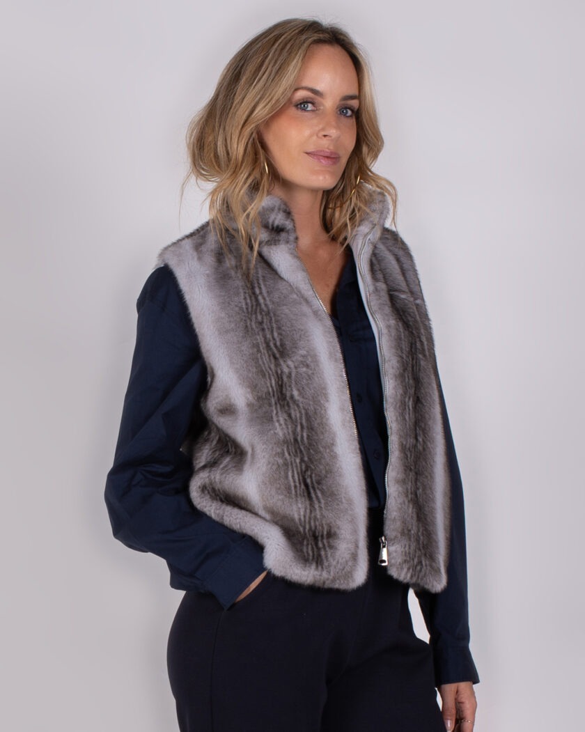 Vrouw draagt een chique grijze bont-look bodywarmer uit de Studio AW25-26 collectie over een donkerblauwe blouse.