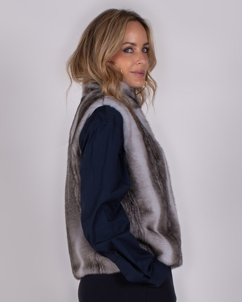 Vrouw met halflang blond haar draagt een grijsbruine bontlook bodywarmer uit de Studio AW25-26 collectie.