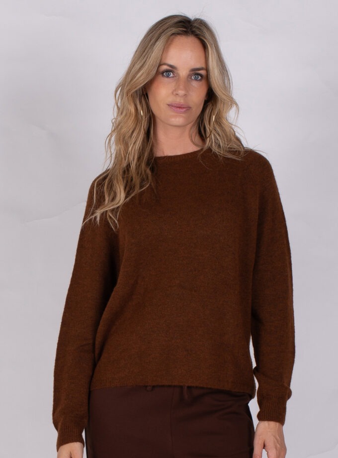 Vrouw draagt een donkerbruine trui uit de Studio AW25-26 collectie tegen een neutrale achtergrond.