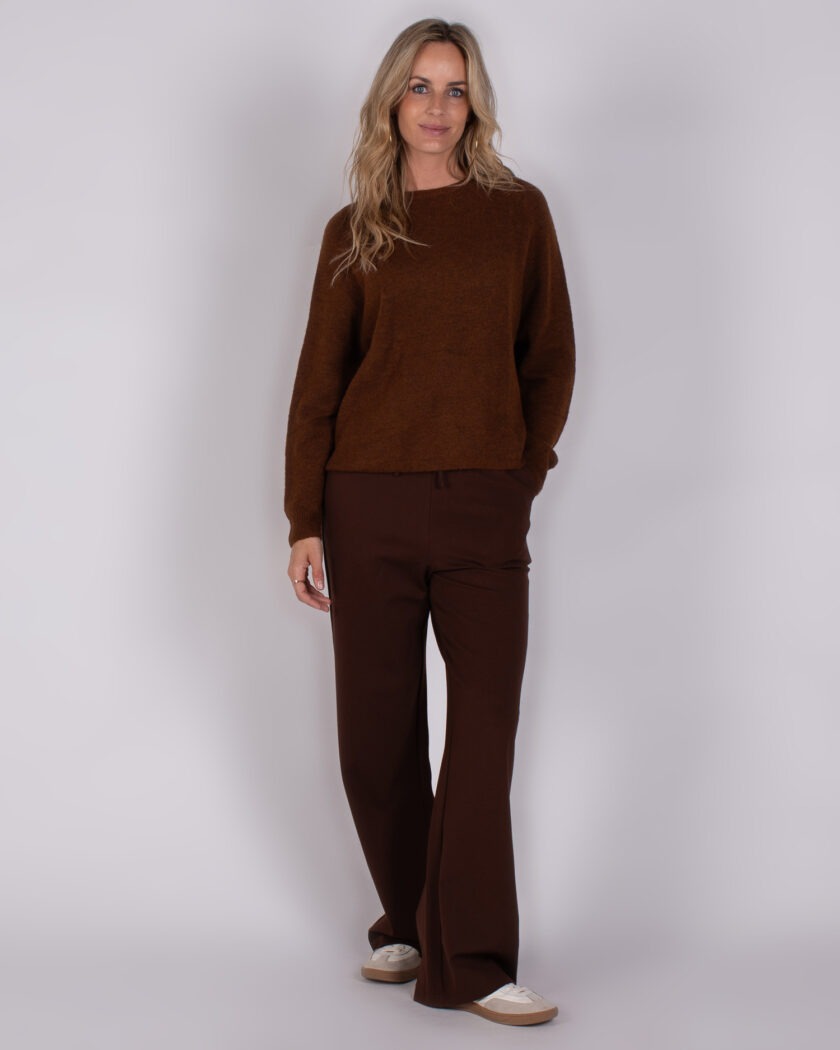 Vrouw draagt een bruine trui en bijpassende wijde broek uit de Studio AW25-26 collectie.