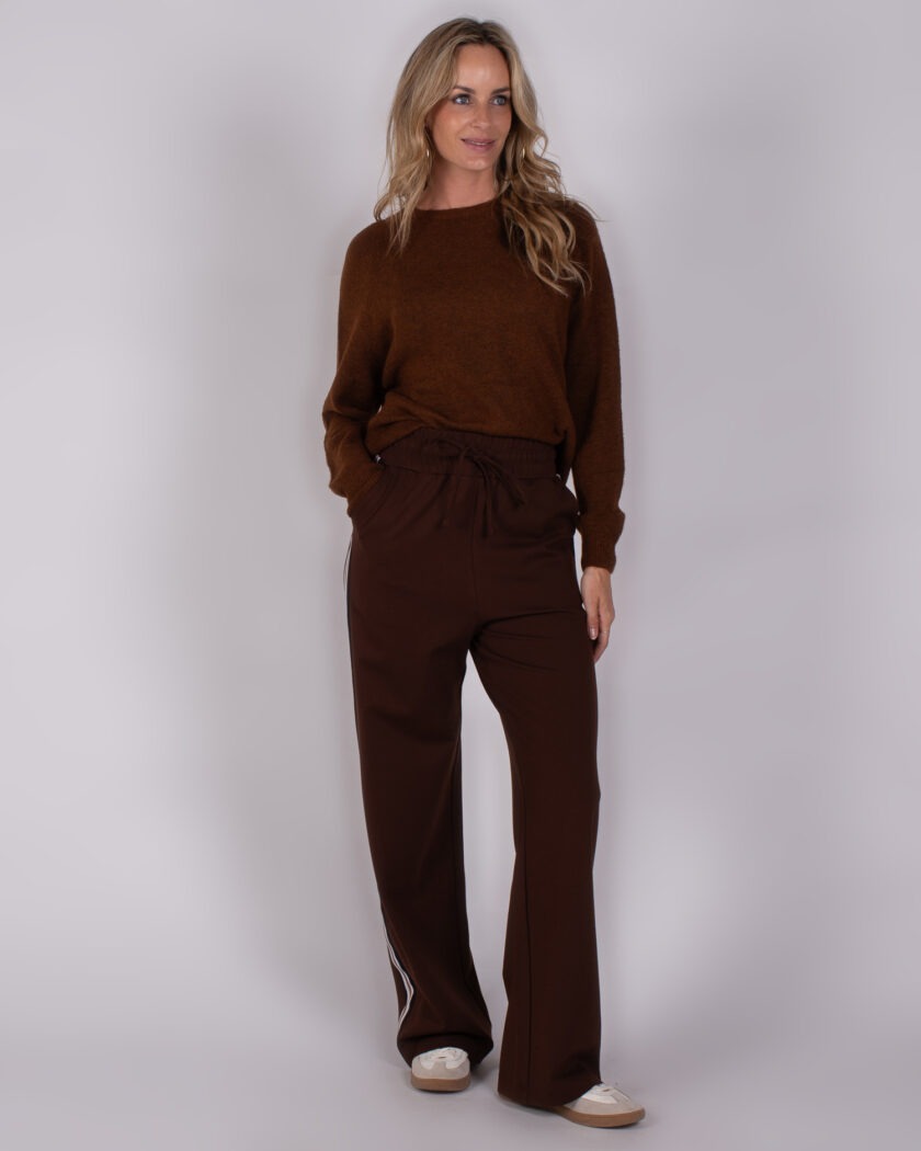 Vrouw draagt een comfortabele, donkerbruine outfit bestaande uit een trui en wijde broek met sportieve details uit de Studio AW25-26 collectie.