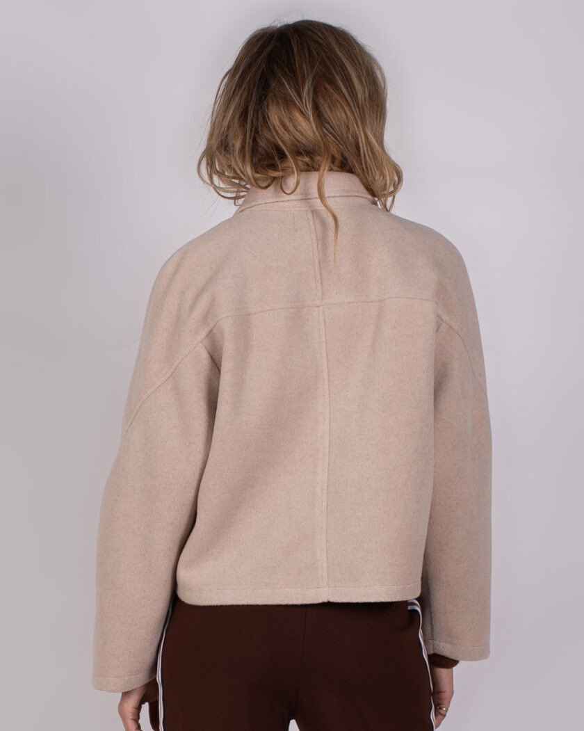 Achteraanzicht van een model dat een beige jas uit de Studio AW25/26-collectie draagt.