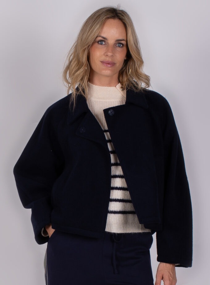 Vrouw draagt een donkerblauwe jas over een gestreepte trui uit de Studio AW25-26-13 collectie.