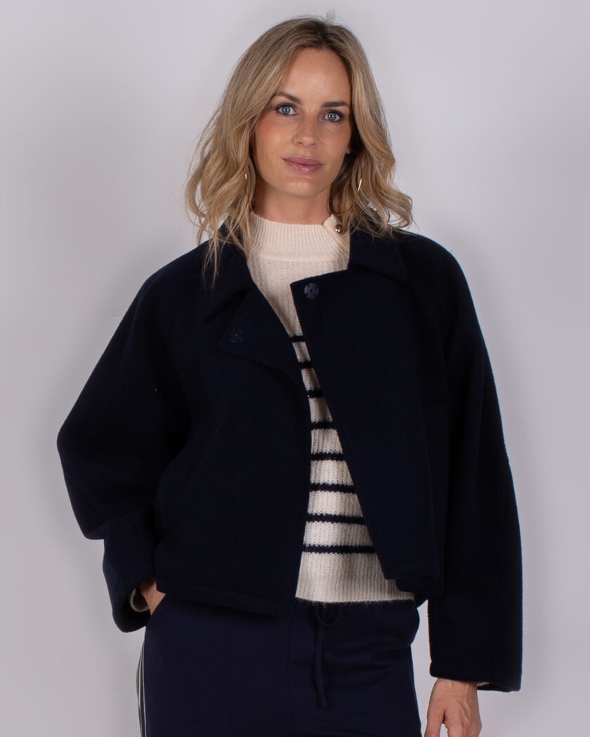Vrouw draagt een donkerblauwe jas over een gestreepte trui uit de Studio AW25-26-13 collectie.