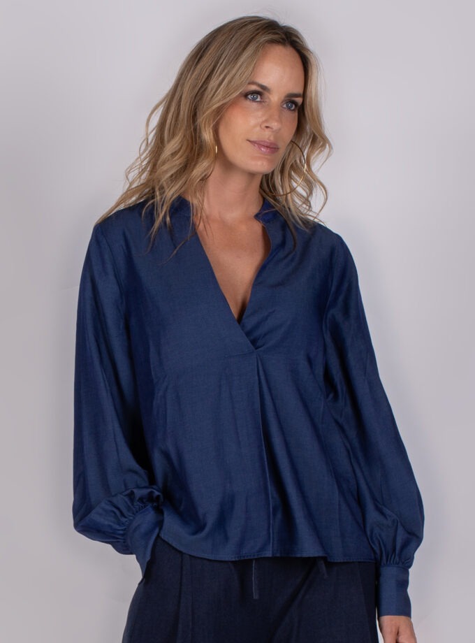 Vrouw draagt een donkerblauwe blouse met V-hals en ballonmouwen uit de Studio AW25-26-130 collectie.