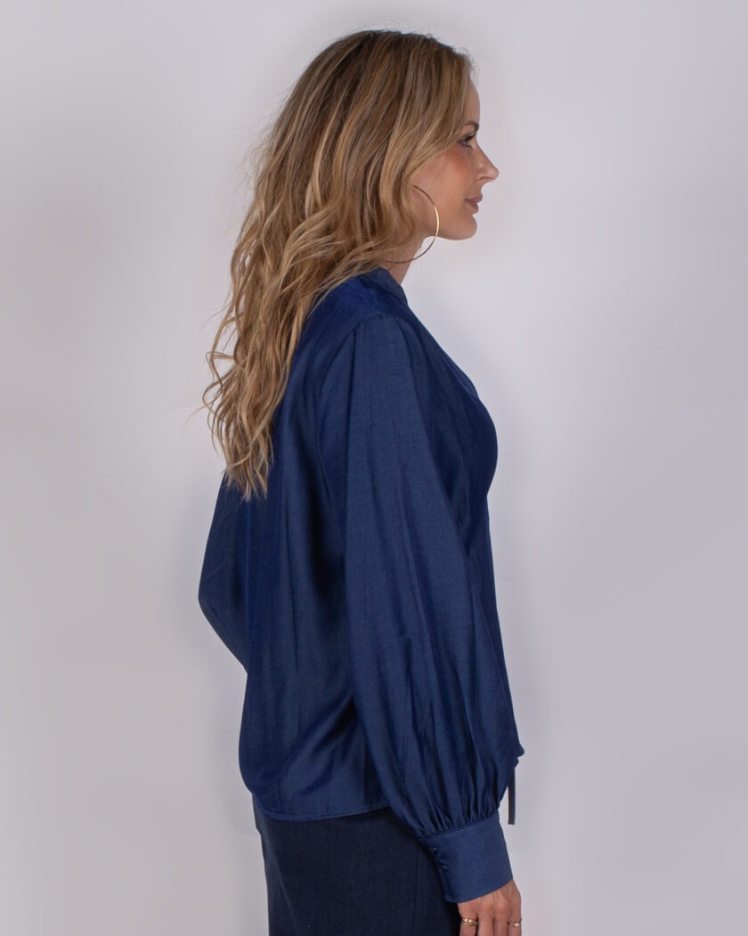 Vrouw in zijaanzicht draagt een donkerblauwe blouse met lange pofmouwen uit de Studio AW25-26 collectie.
