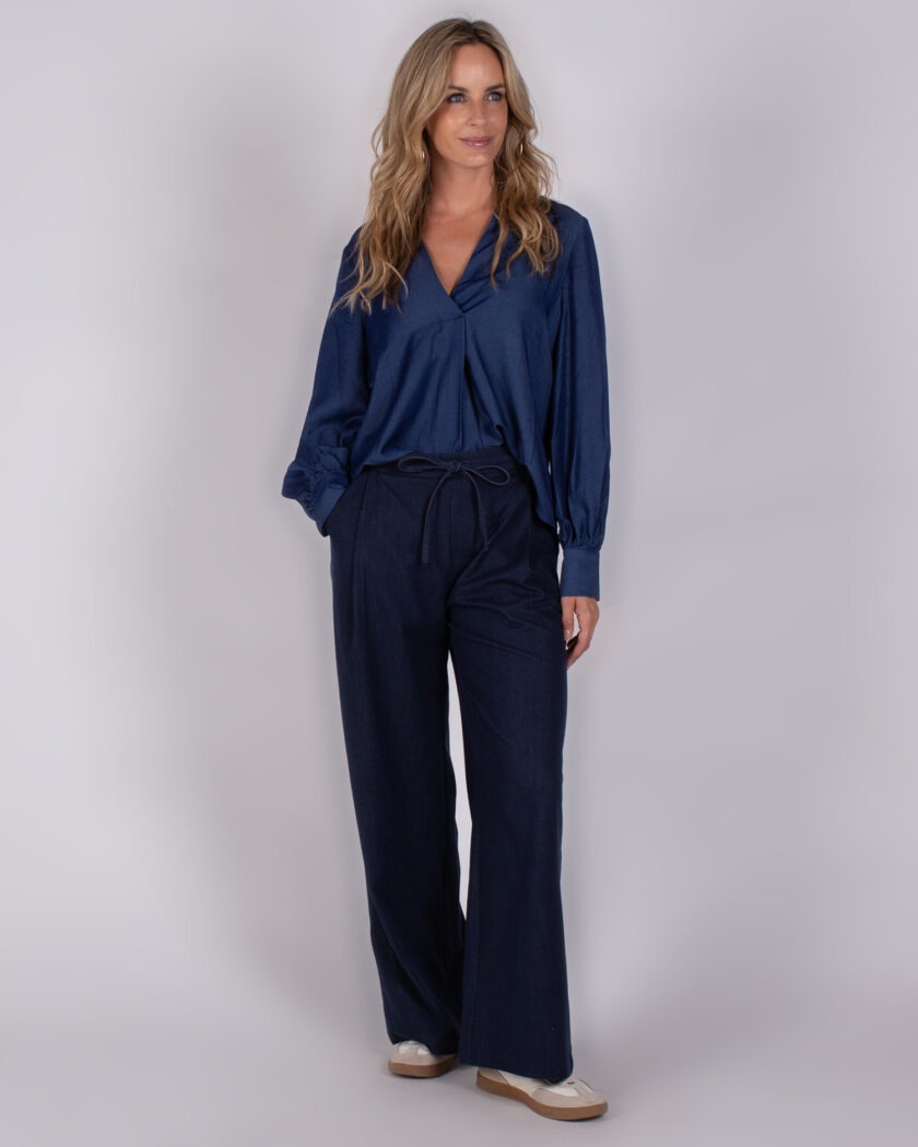 Vrouw draagt een donkerblauwe blouse met V-hals en wijde broek uit de Studio AW25-26 collectie.