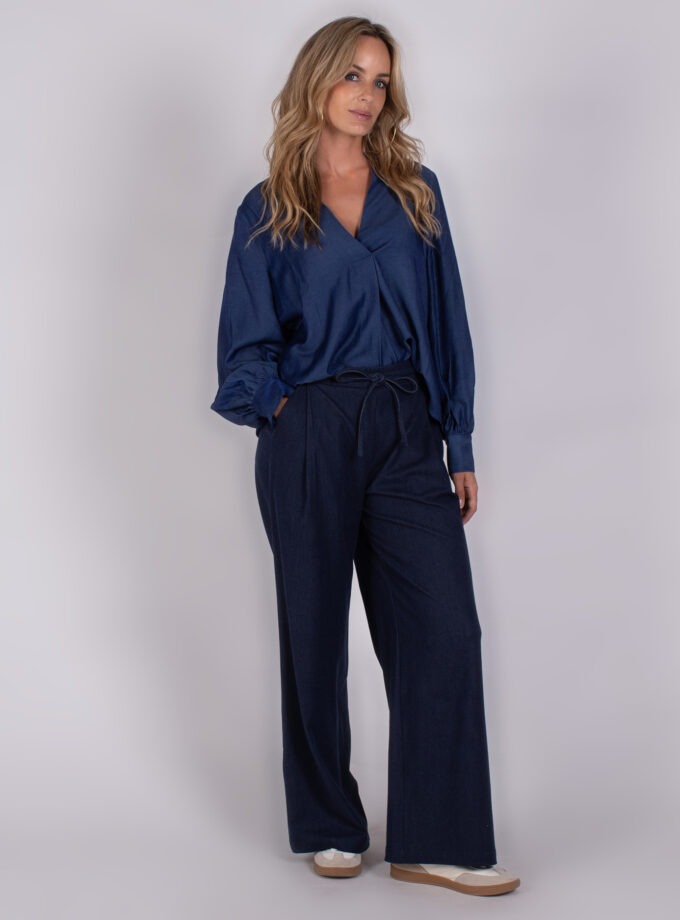 Vrouw draagt een donkerblauwe blouse met lange mouwen en een wijde broek uit de Studio_AW25-26-134 collectie.