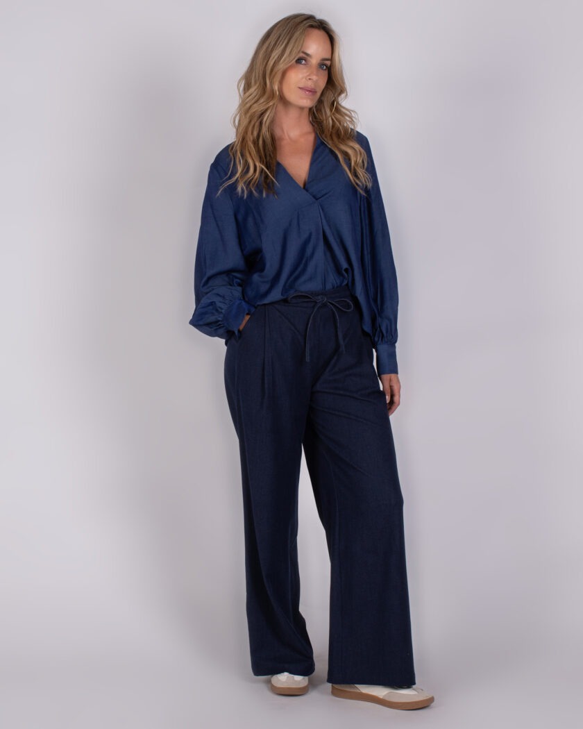 Vrouw draagt een donkerblauwe blouse met lange mouwen en een wijde broek uit de Studio_AW25-26-134 collectie.