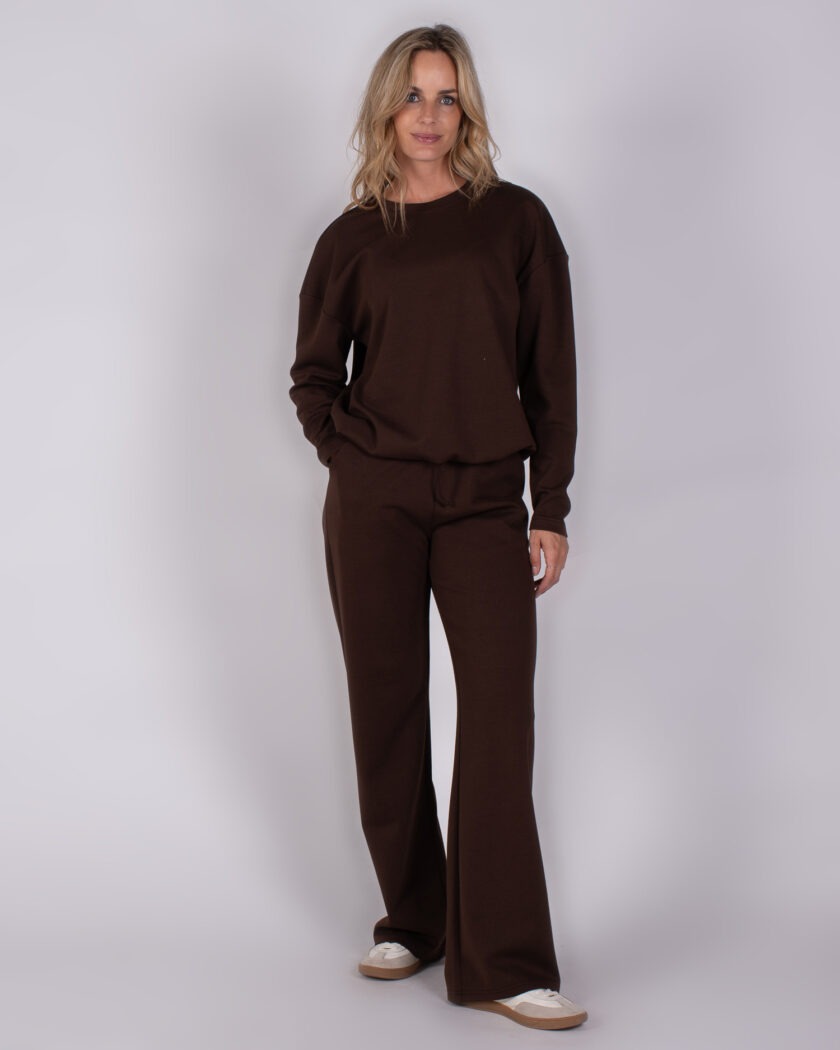 Vrouw draagt een donkerbruin loungepak met wijde broekspijpen uit de Studio AW25-26 collectie.
