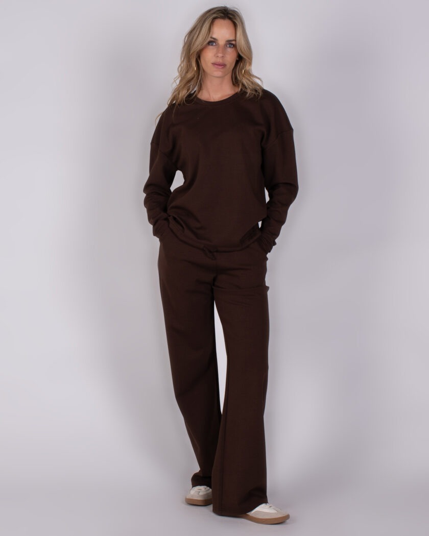 Vrouw draagt een donkerbruin loungepak met wijde broek en sneakers uit de Studio AW25-26 collectie.