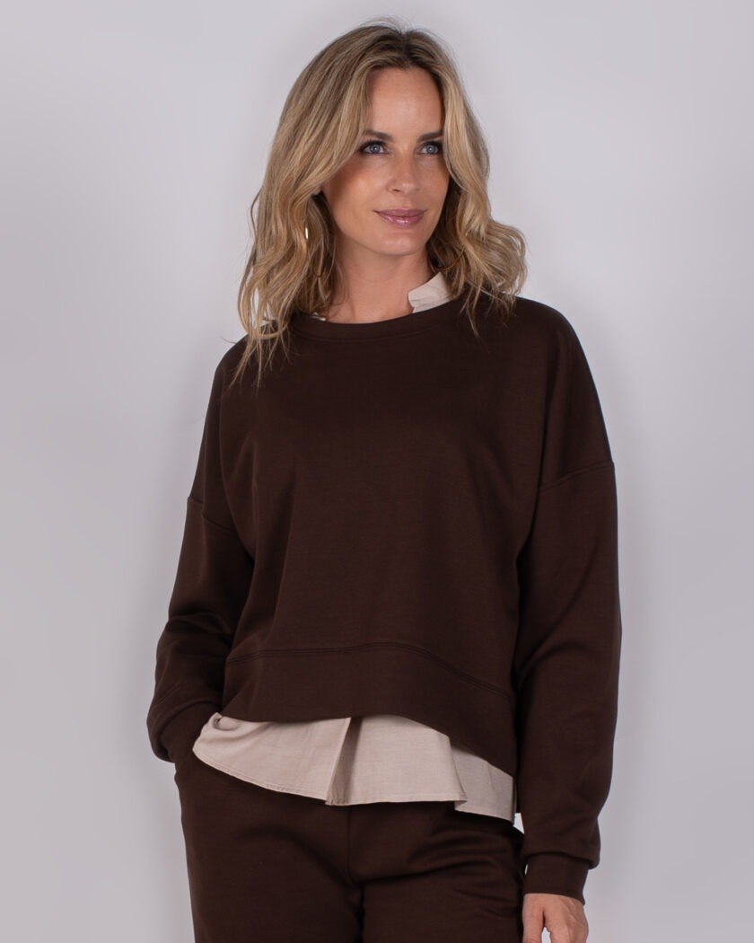Vrouw draagt een donkerbruine sweater met beige blouse eronder uit de Studio AW25-26 collectie.
