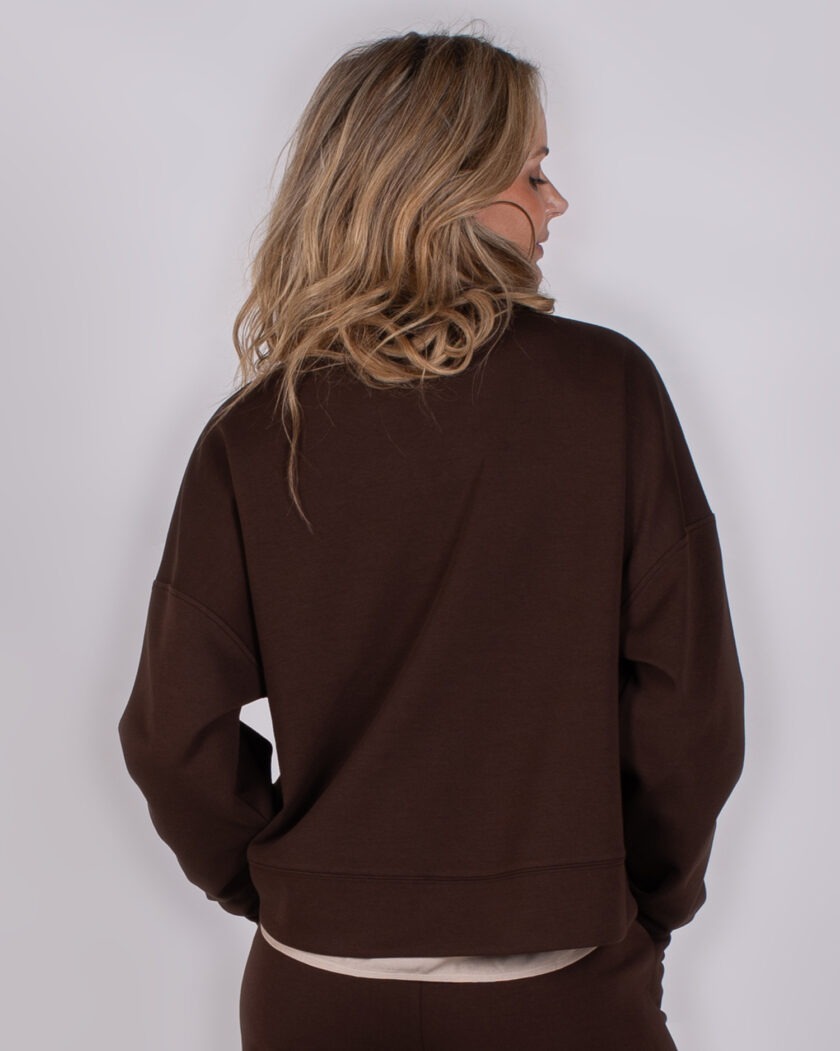 Vrouw van achteren in een donkerbruine trui en broek uit de Studio AW25-26 collectie.