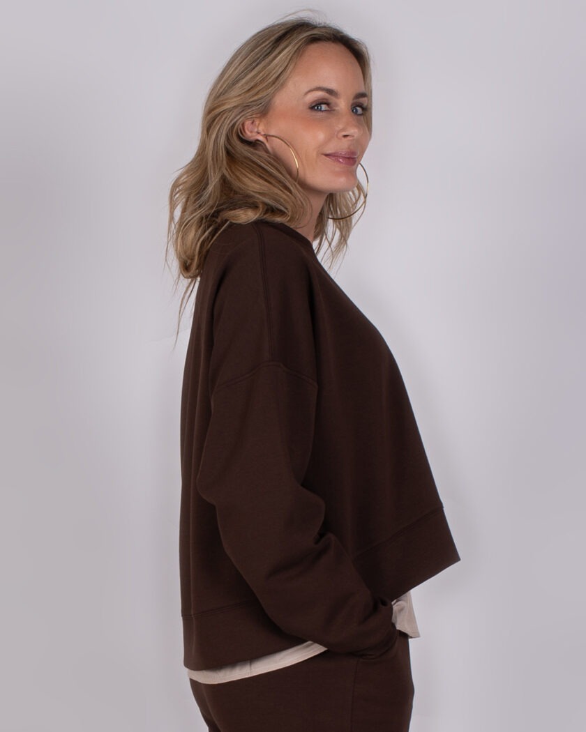 Vrouw in zijaanzicht draagt een donkerbruine trui uit de Studio AW25-26 collectie.