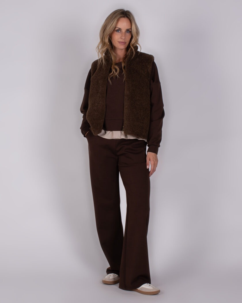 Vrouw in een bruine lounge-outfit met wijde broek, sweater en teddy bodywarmer uit Studio AW25-26 collectie.