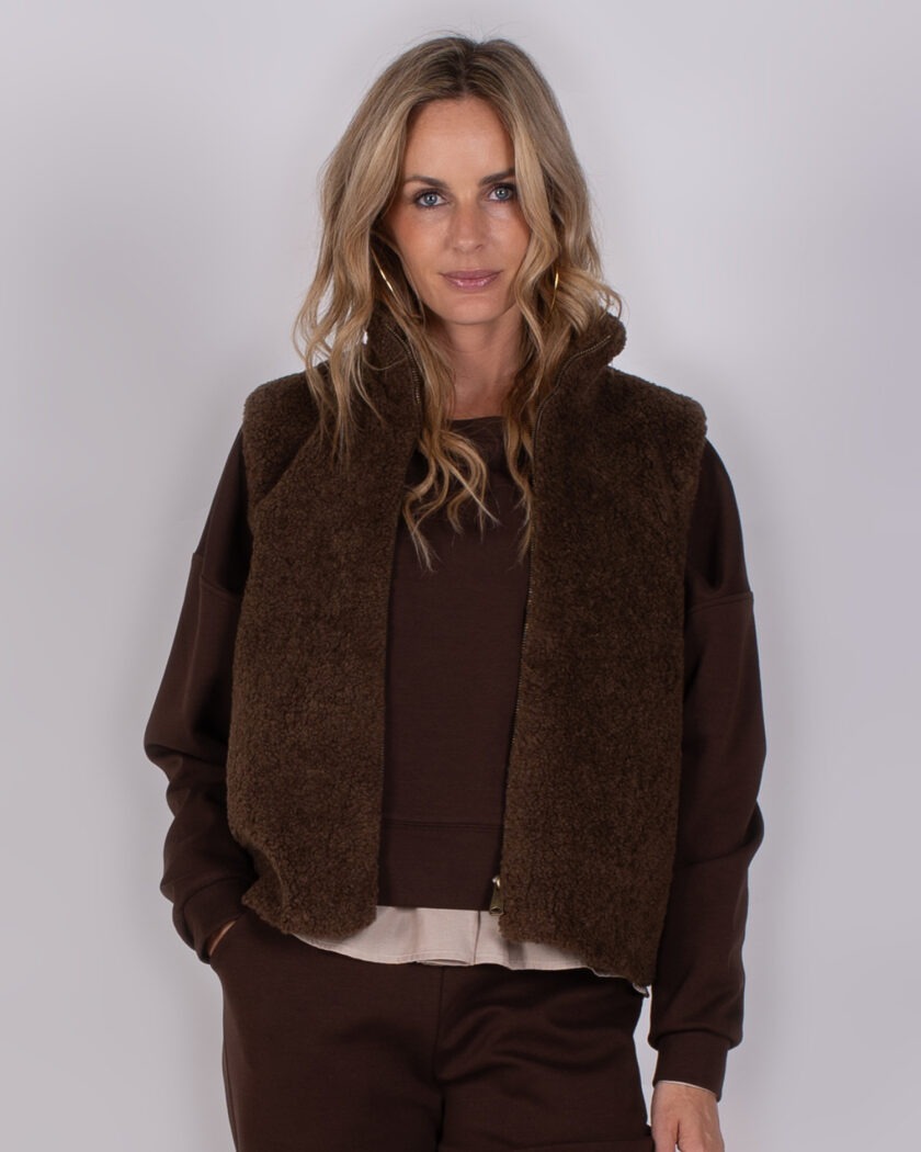 Vrouw in bruine Studio AW25-26-186 outfit met teddy bodywarmer en sweatshirt.