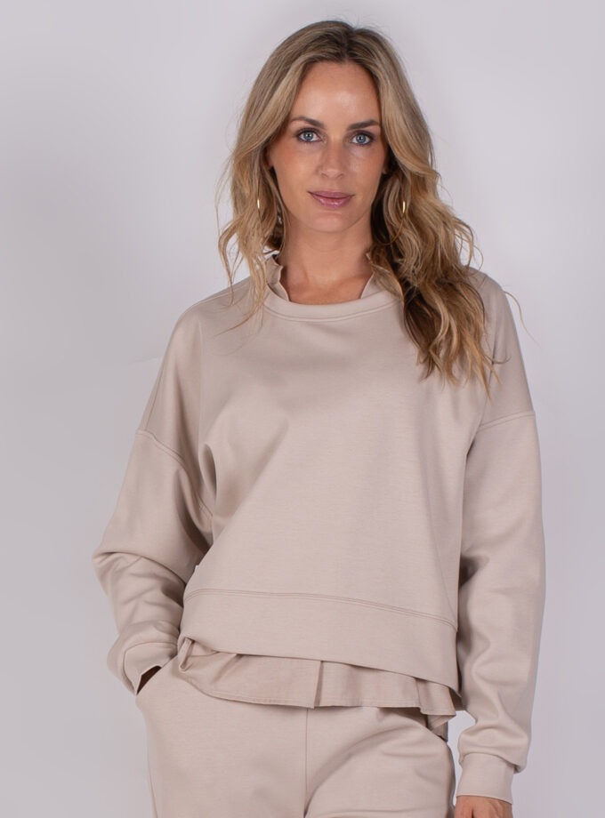 Vrouw draagt een beige lounge-outfit bestaande uit een comfortabele sweater en bijpassende broek uit de Studio AW25-26 collectie.