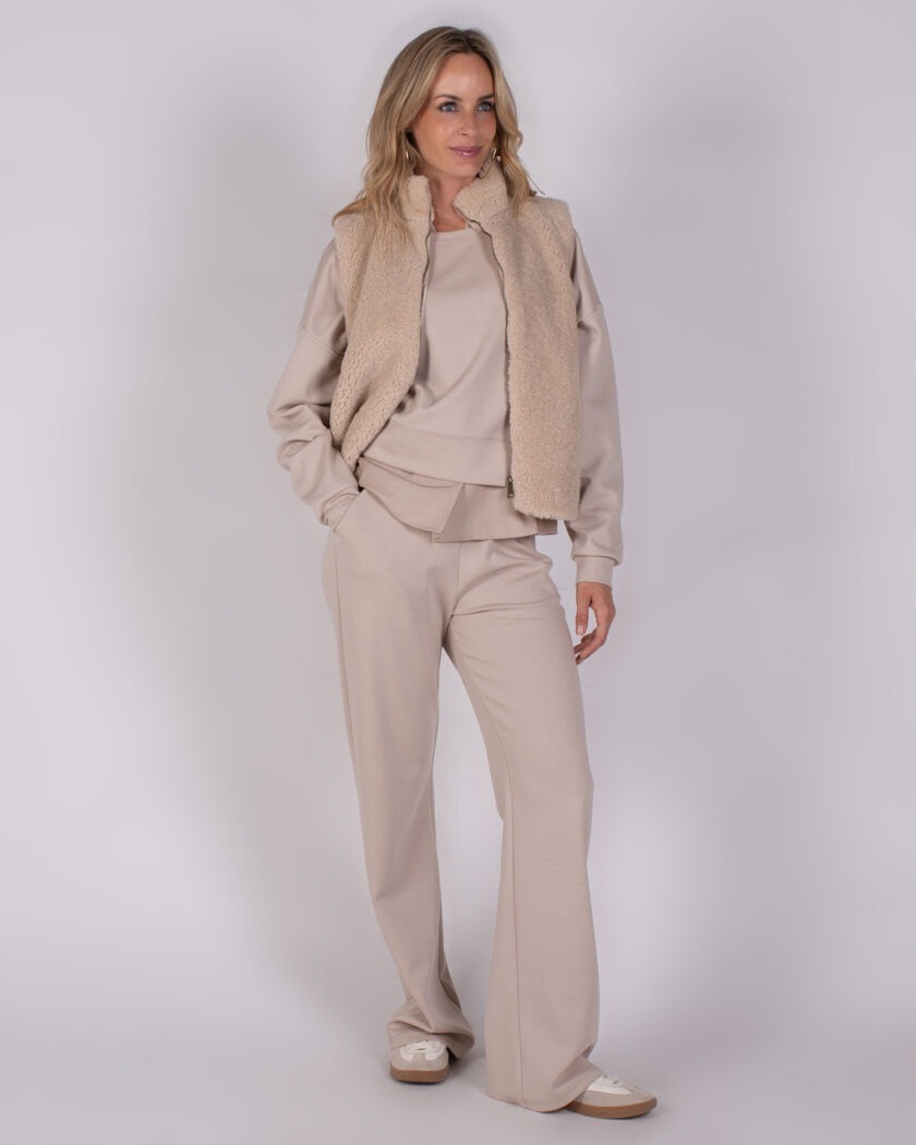 Vrouw in beige loungepak met bijpassend fleece bodywarmer uit de Studio AW25-26 collectie.