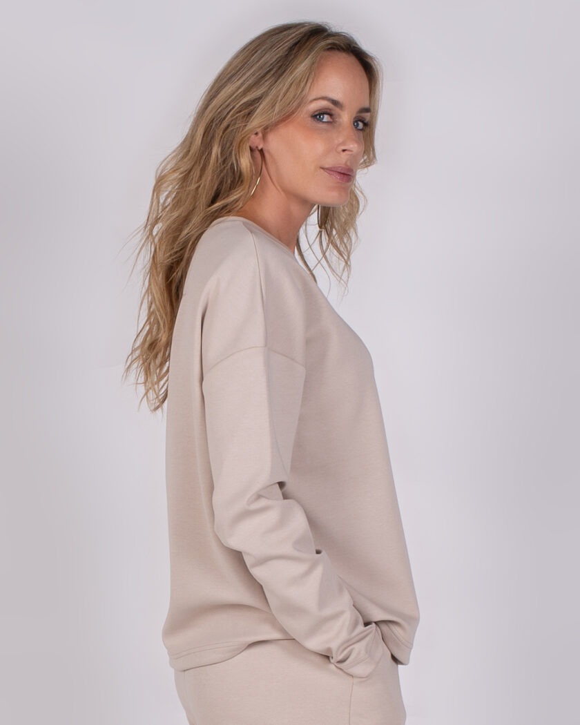 Vrouw in beige loungepak uit de Studio AW25-26 collectie, poseert in zijaanzicht.