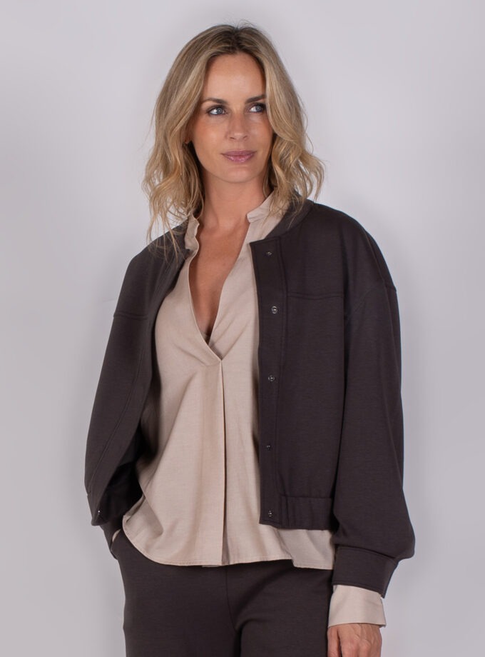 Vrouw draagt een donkerbruine bomberjack met bijpassende broek en beige blouse uit de Studio AW25-26-205 collectie.