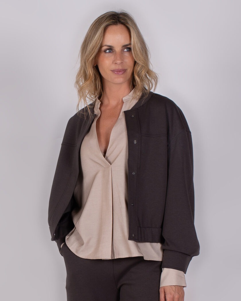 Vrouw draagt een donkerbruine bomberjack met bijpassende broek en beige blouse uit de Studio AW25-26-205 collectie.