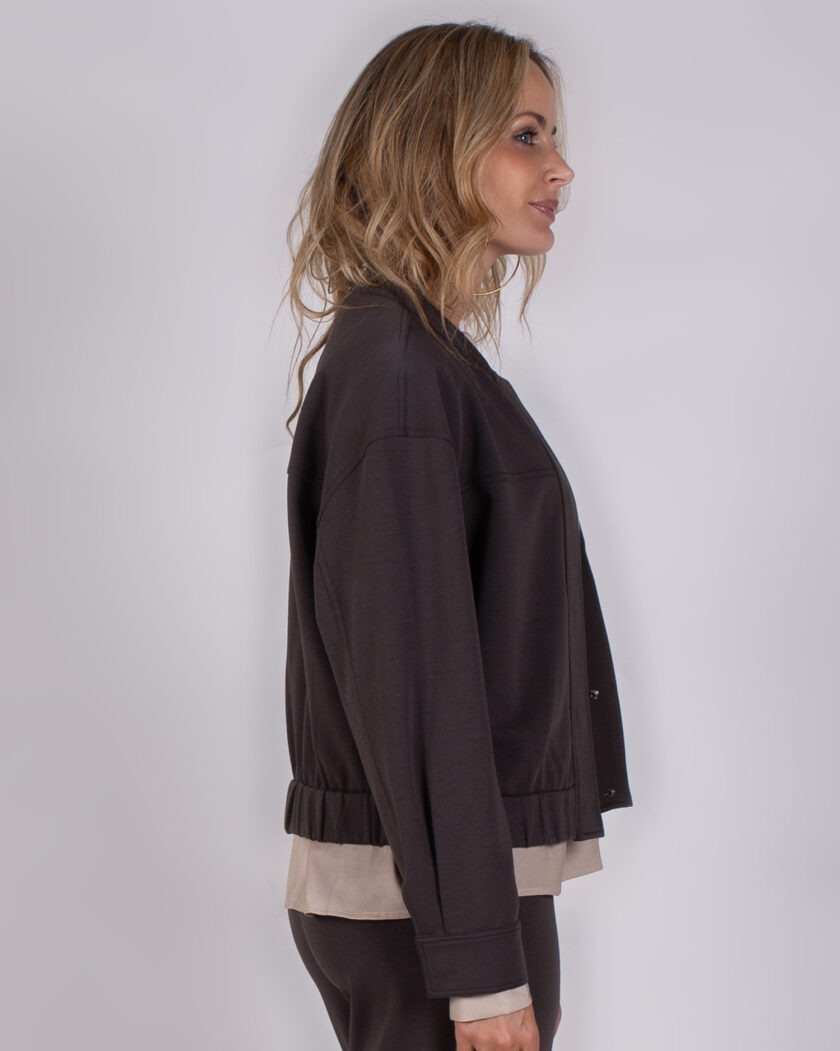 Vrouw in zijaanzicht draagt een donkerbruine Studio AW25-26-207 jas met beige top eronder.