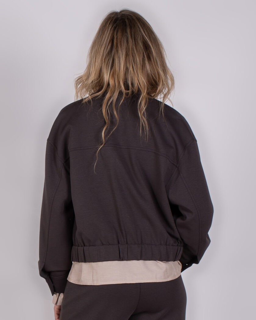 Achteraanzicht van een vrouw in een donkerbruine Studio AW25-26-208 outfit met loshangend haar.