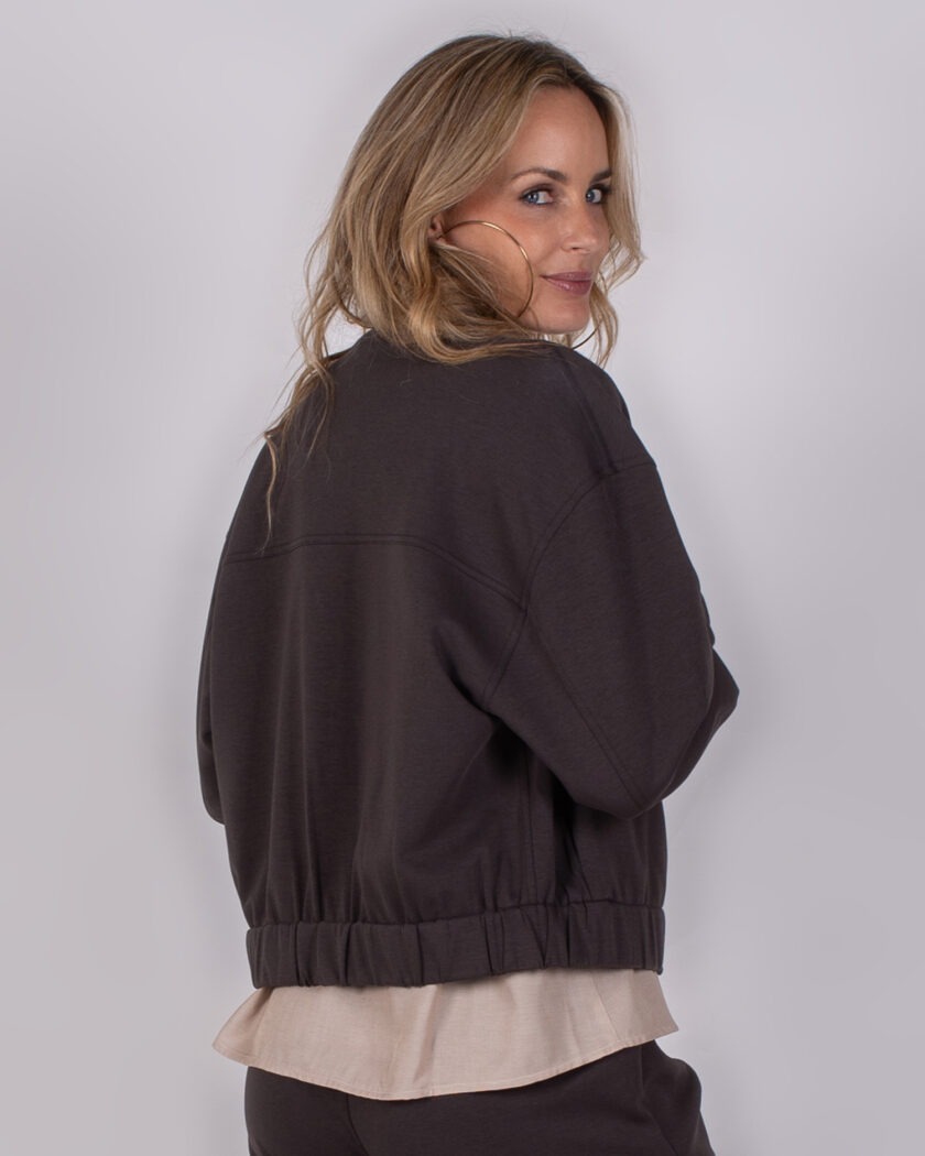 Vrouw draagt een donkerbruine Studio AW25-26-209 jas met beige blouse eronder en kijkt over haar schouder.