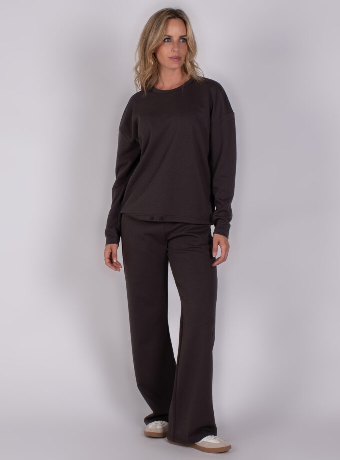 Vrouw draagt een donkerbruin loungepak met wijde broek en lange mouwen uit de Studio AW25-26-211 collectie.