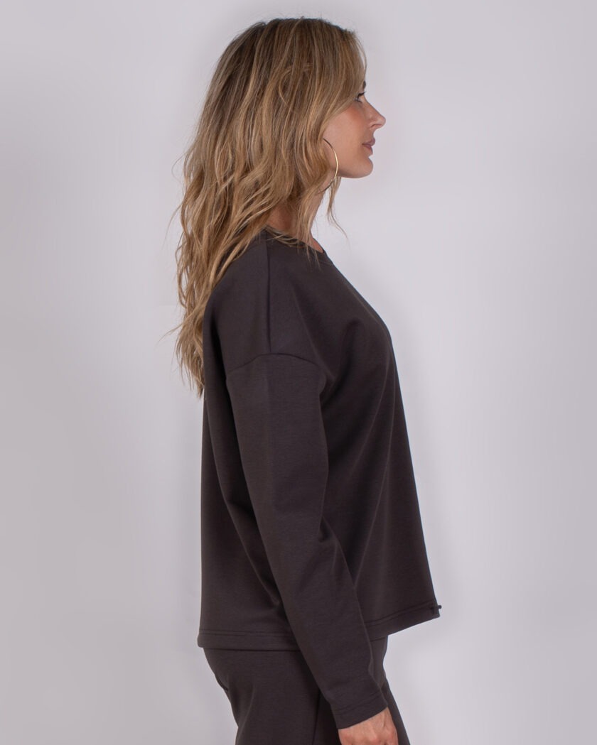 Vrouw in profiel die een donkergrijze, lange mouwen top en bijpassende broek draagt uit de Studio AW25-26 collectie.