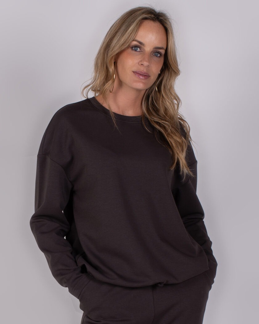 Vrouw draagt een donkerbruine sweater van Studio AW25-26-214 en poseert tegen een neutrale achtergrond.