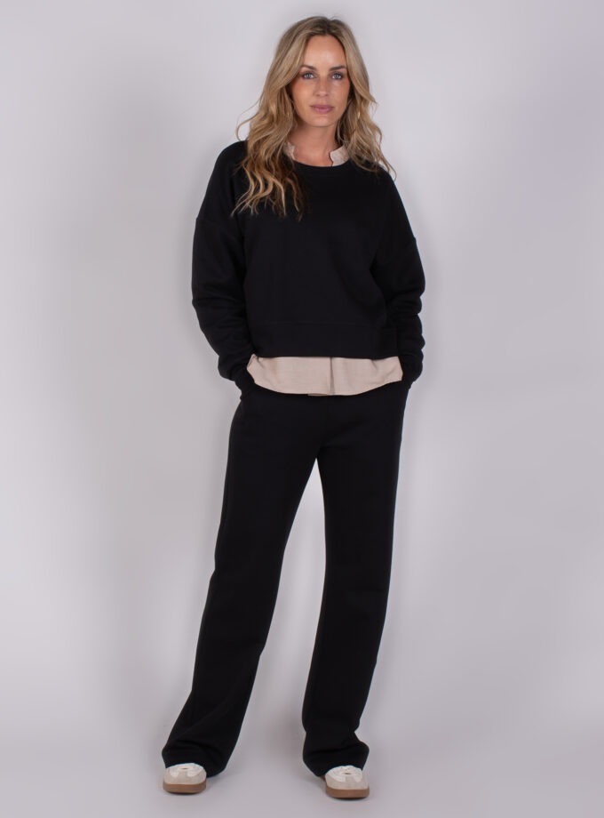 Vrouw draagt een zwarte loungset met beige blouse uit de Studio AW25-26 collectie.
