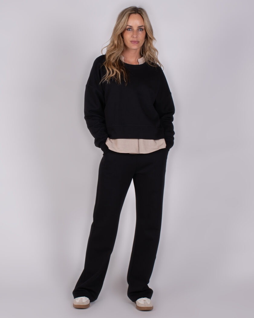 Vrouw draagt een zwarte loungset met beige blouse uit de Studio AW25-26 collectie.