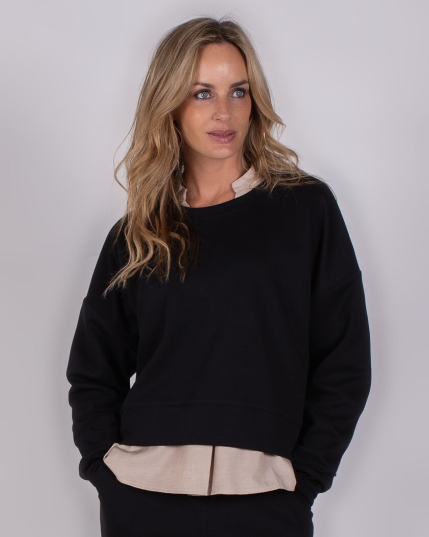 Vrouw draagt een zwarte trui met beige blouse eronder uit de Studio AW25-26 collectie.