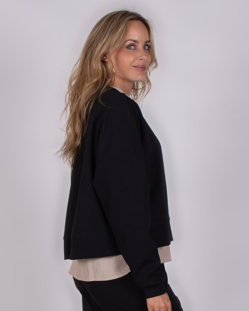 Vrouw met lang blond haar draagt een zwarte trui uit de Studio AW25-26-218 collectie.