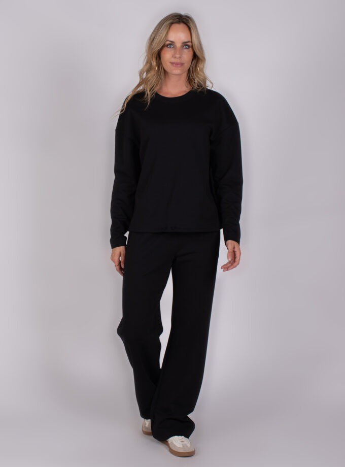 Vrouw draagt een zwarte Studio AW25-26-221 loungewear-set met lange mouwen en wijde broek.