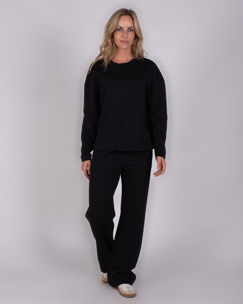 Vrouw draagt een zwarte Studio AW25-26-221 loungewear-set met lange mouwen en wijde broek.