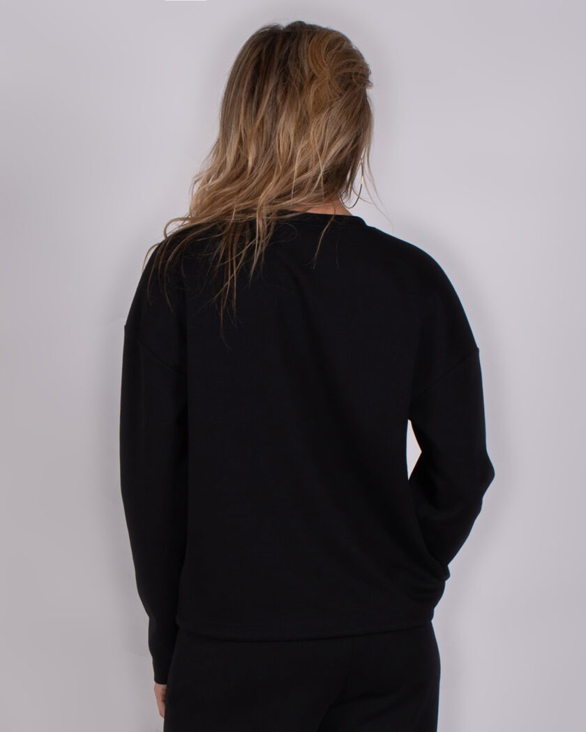 Achteraanzicht van een persoon die een zwarte trui uit de Studio AW25-26 collectie draagt.